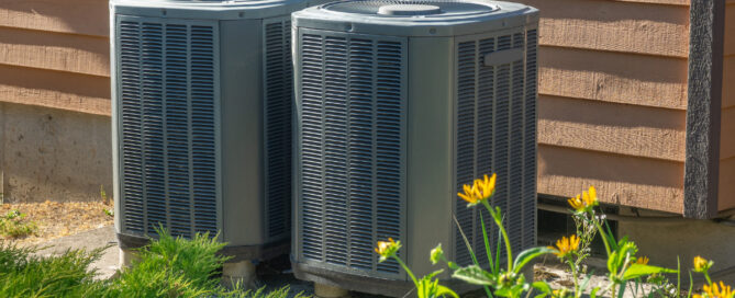 Two HVAC systems placed outside a home surrounded by grass and yellow flowers
