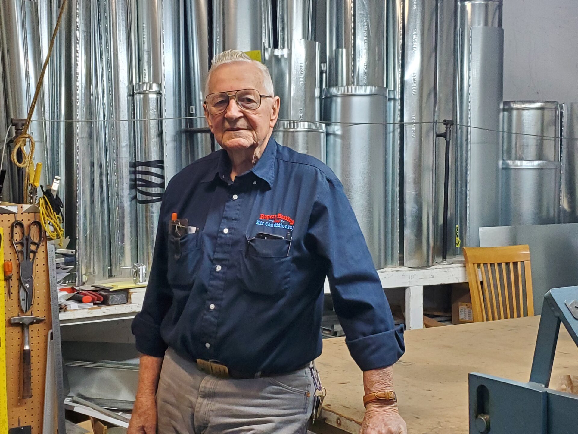 Fred Roper leaning against a table in Roper's Heating and Air Conditioning shop room