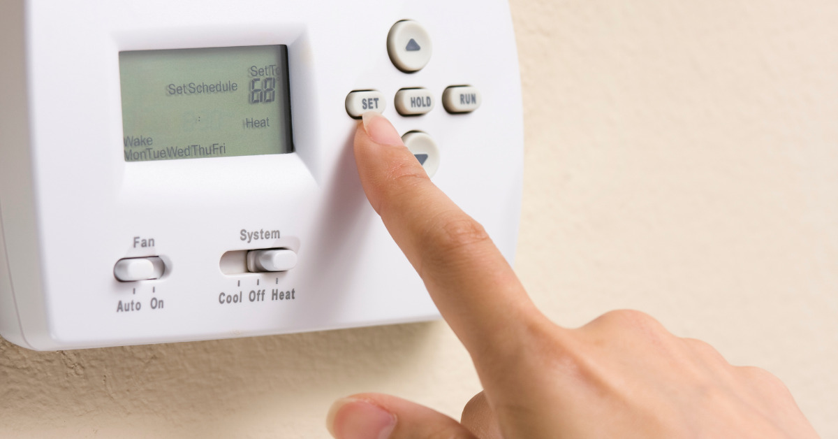 A person's finger touching a button on a thermostat for home comfort